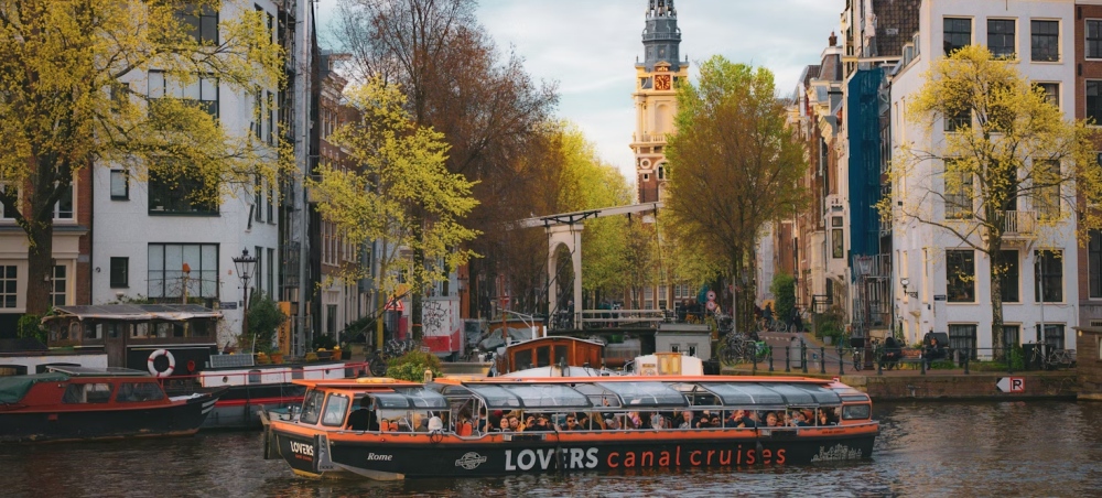 A glass-roofed canal cruise boat moving through Amsterdam.