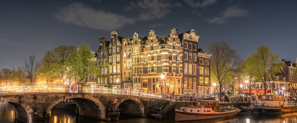 Lit canal houses and a bridge at night in Amsterdam.