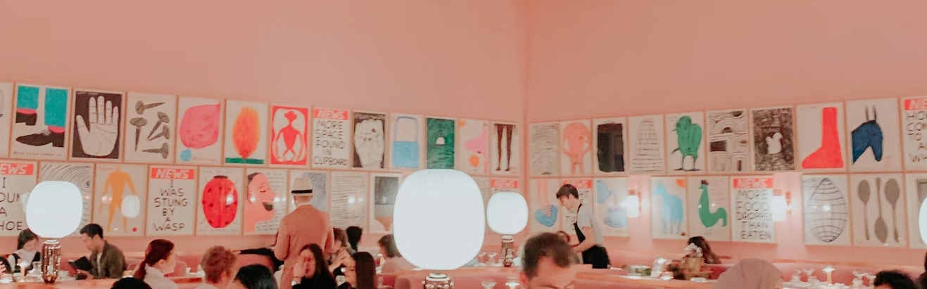 The pink sketch dining room filled with framed art, glowing lamps, and afternoon tea guests.