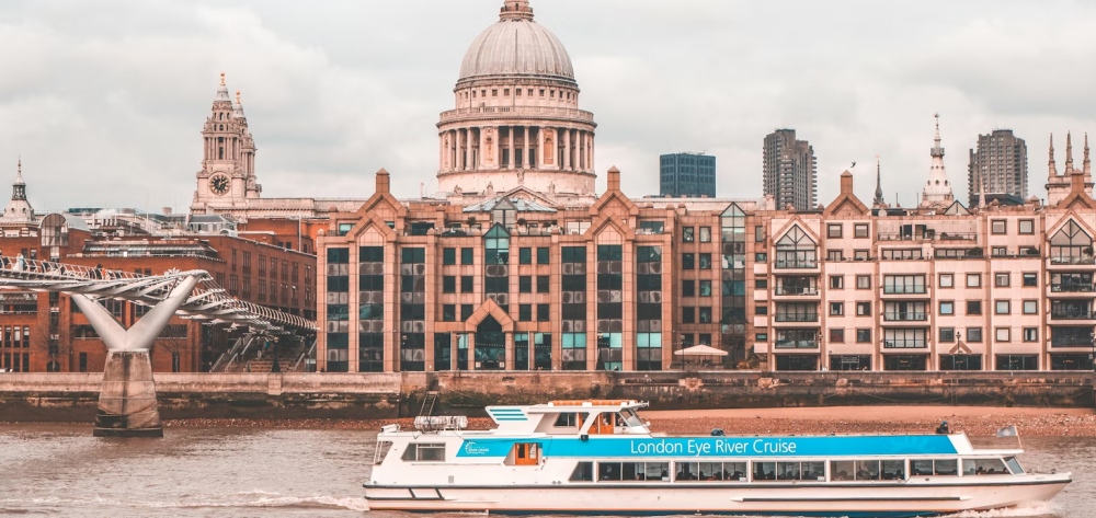 A sightseeing boat cruising along the Thames with London landmarks in view.