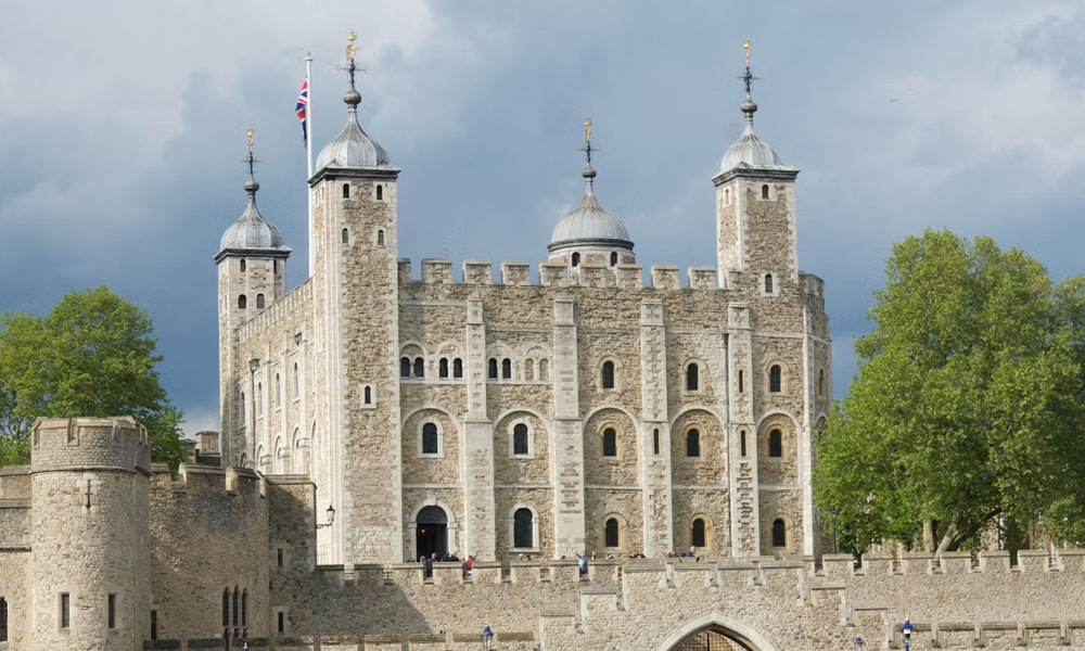 The White Tower and outer walls of the Tower of London seen under a darkening sky.