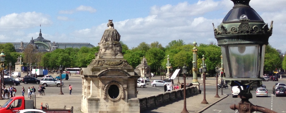 A Paris street scene with statues, ornate lamps, and traffic under a blue sky.