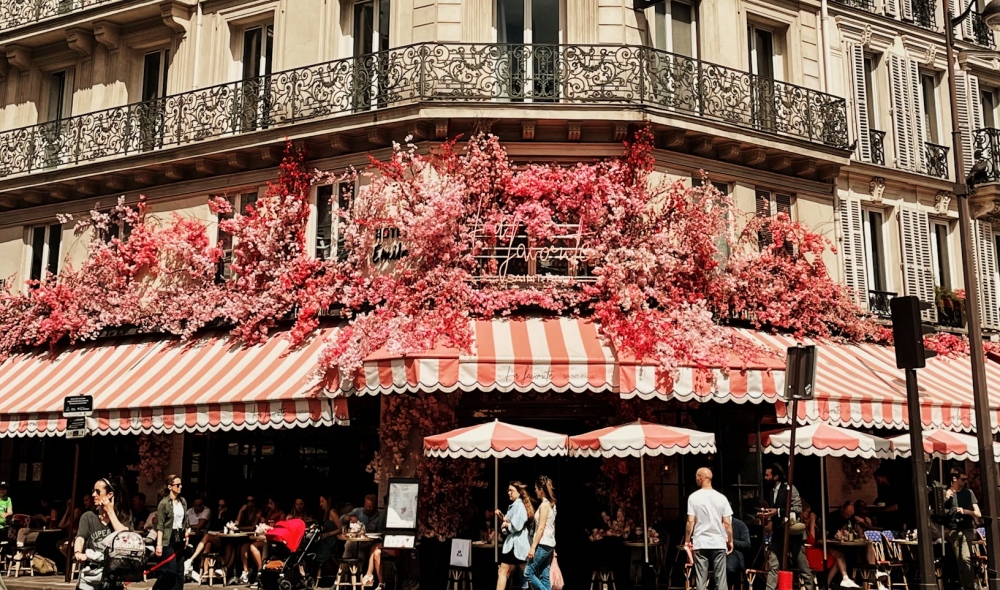 The flower-covered facade of Hotel Emile with striped awnings on a Le Marais street corner.