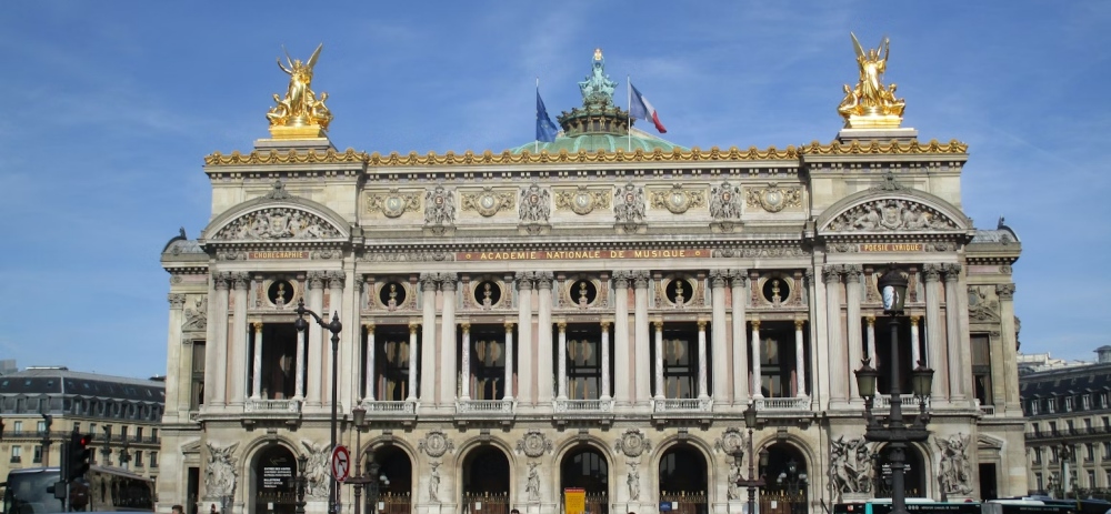 The ornate front facade of the Paris Opera House with gilded statues above the columns.