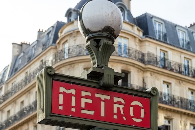 A Paris Metro sign in front of a Haussmann building.