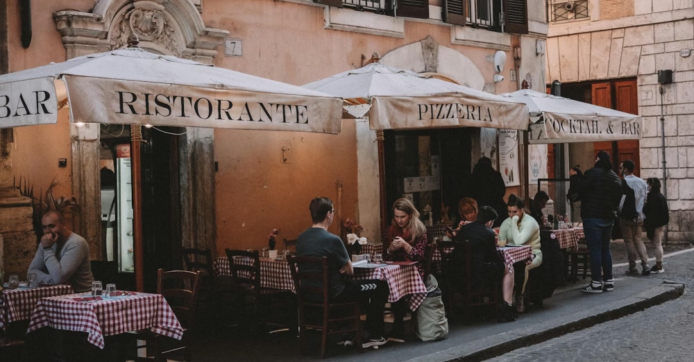 People seated at small restaurant tables on a Rome street.