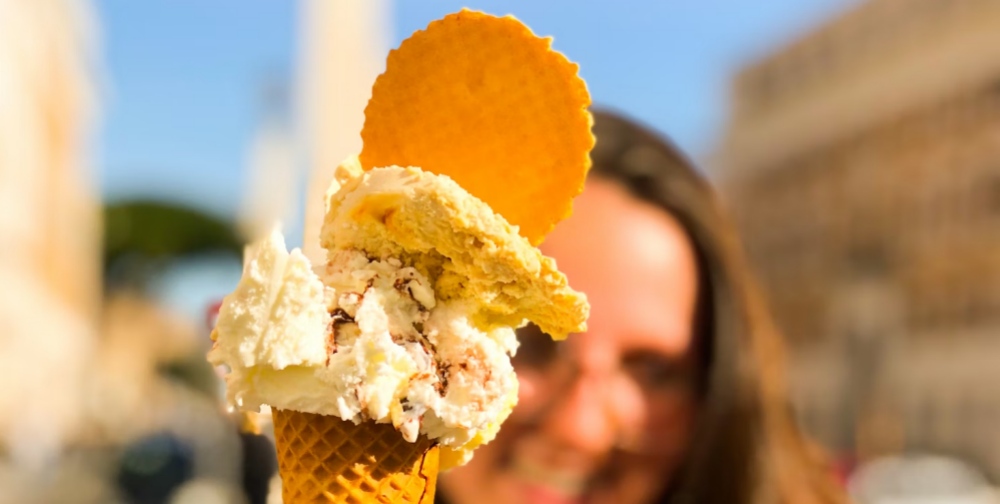 A gelato cone held up with the Colosseum blurred behind it.