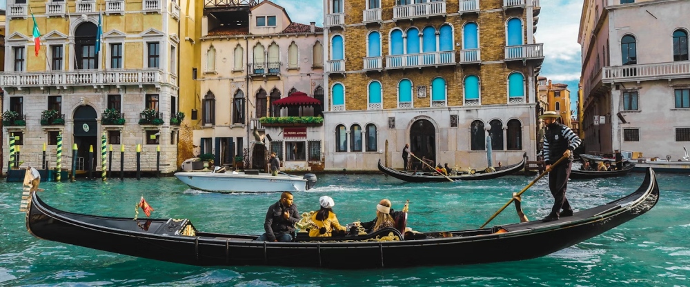 A gondolier steering passengers along a bright Venice canal.