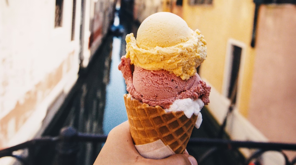 A hand holding a gelato cone above a Venice canal.